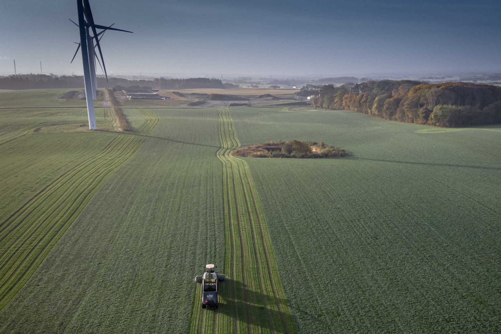 Dronefoto af en traktor, der kører over en græsmark