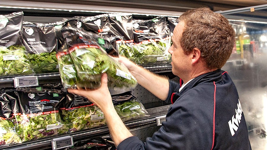 En medarbejder i Kvickly lægger spinat på en hylde i frugt- og grøntafdelingen