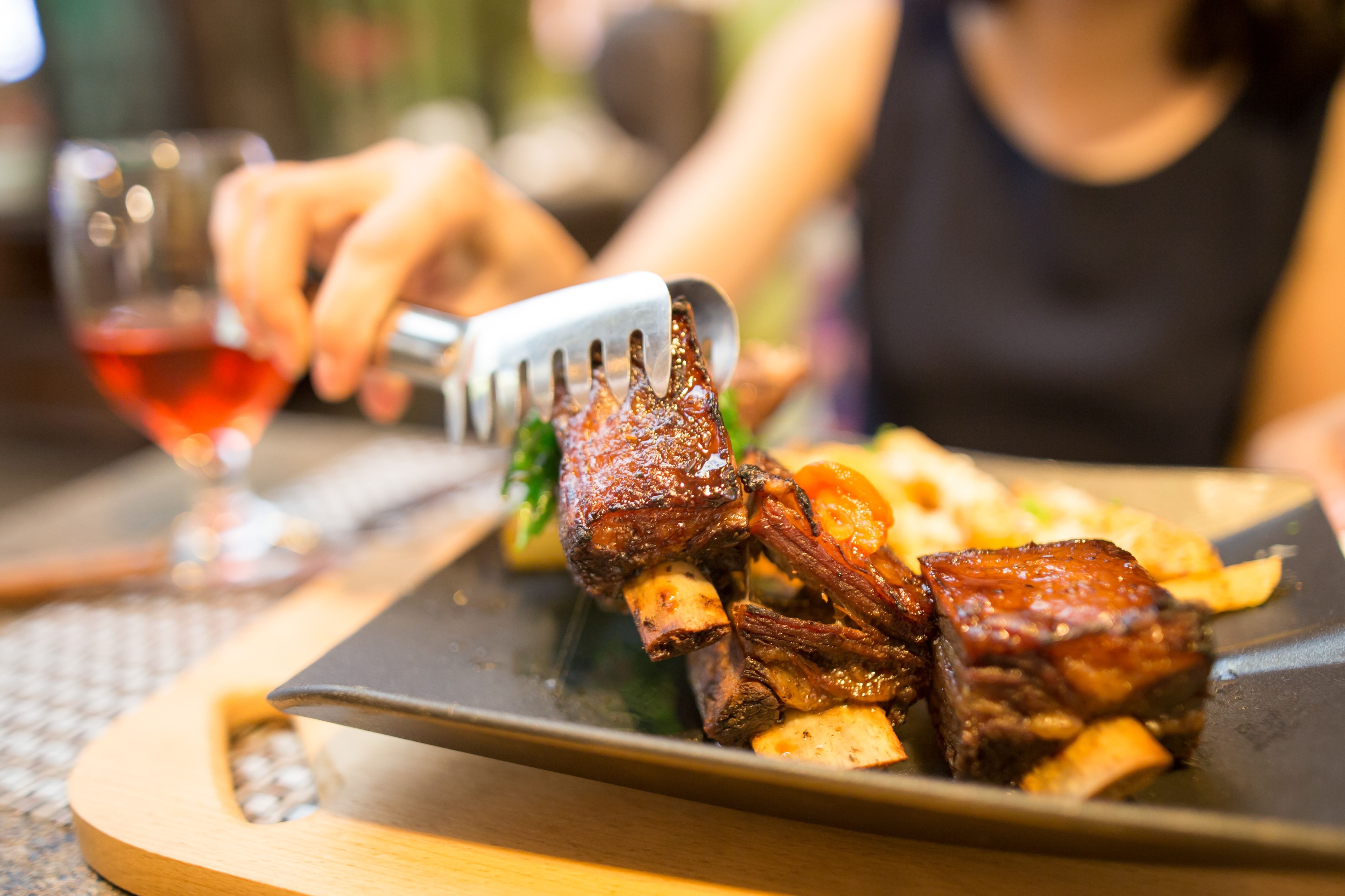En kvinde sidder på en restaurant og tager et stykke kød fra et fad