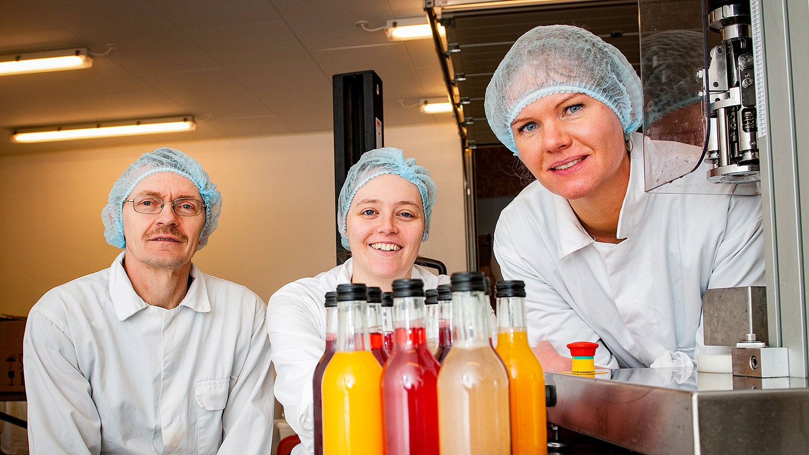 Niels-Christian Bach sidder med datteren Stine Bach Nielsen og produktudvikler Tine Dahl (t.h.) i et lokale, hvor deres flasker står på et bord foran dem