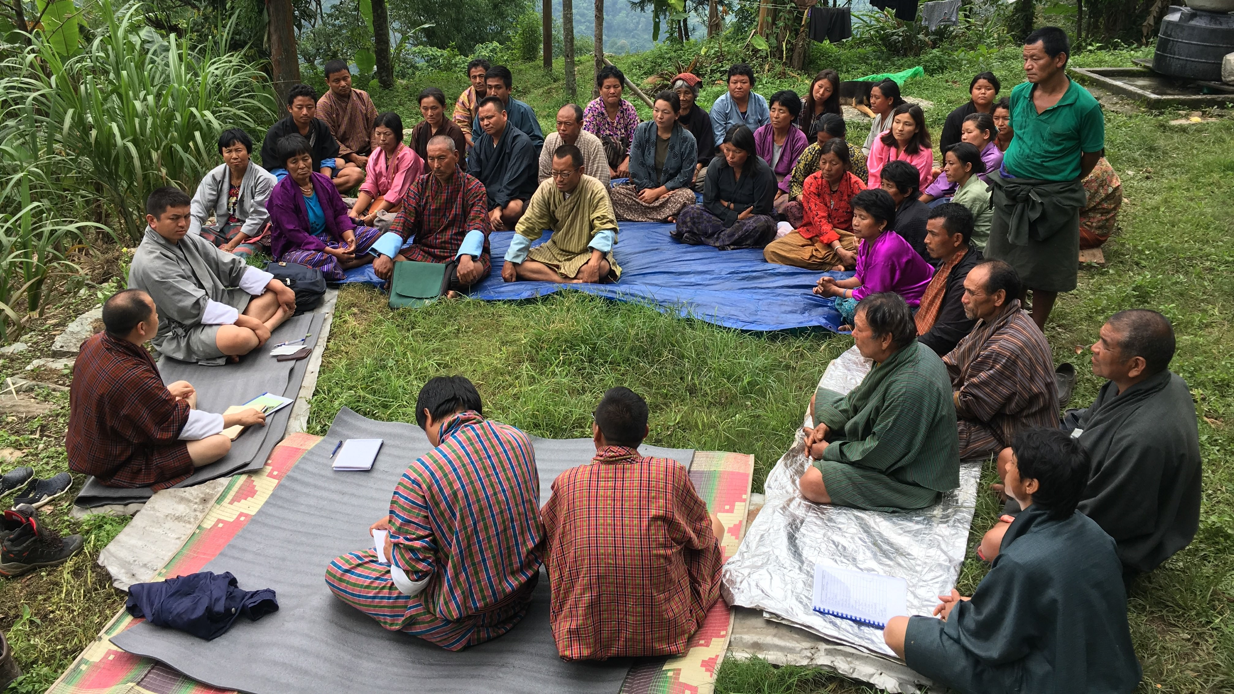 En gruppe bønder sidder i en rundkreds og lytter til en oplægsholder i Bhutan