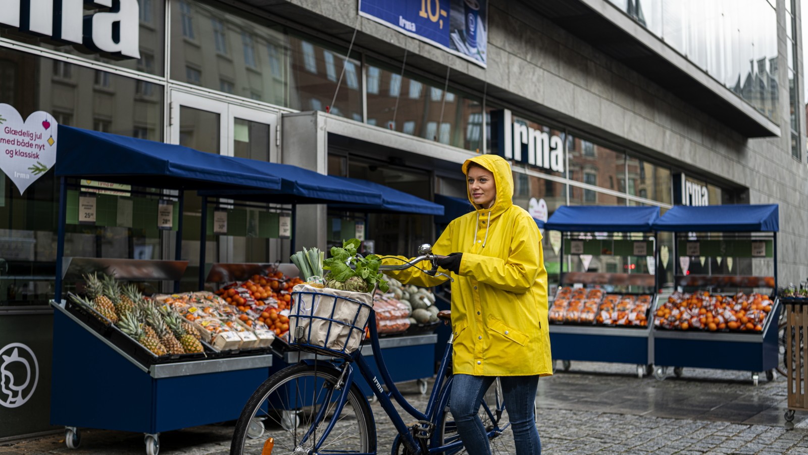 Kunde trækker cykel med fyldt cykelkurv foran Irma-butik.