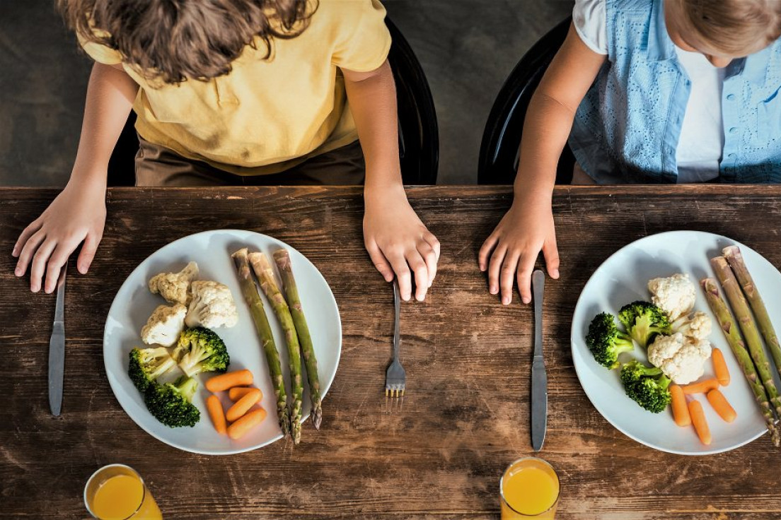 To børn sidder ved et spisebord med tallerkener fyldt med grønsager