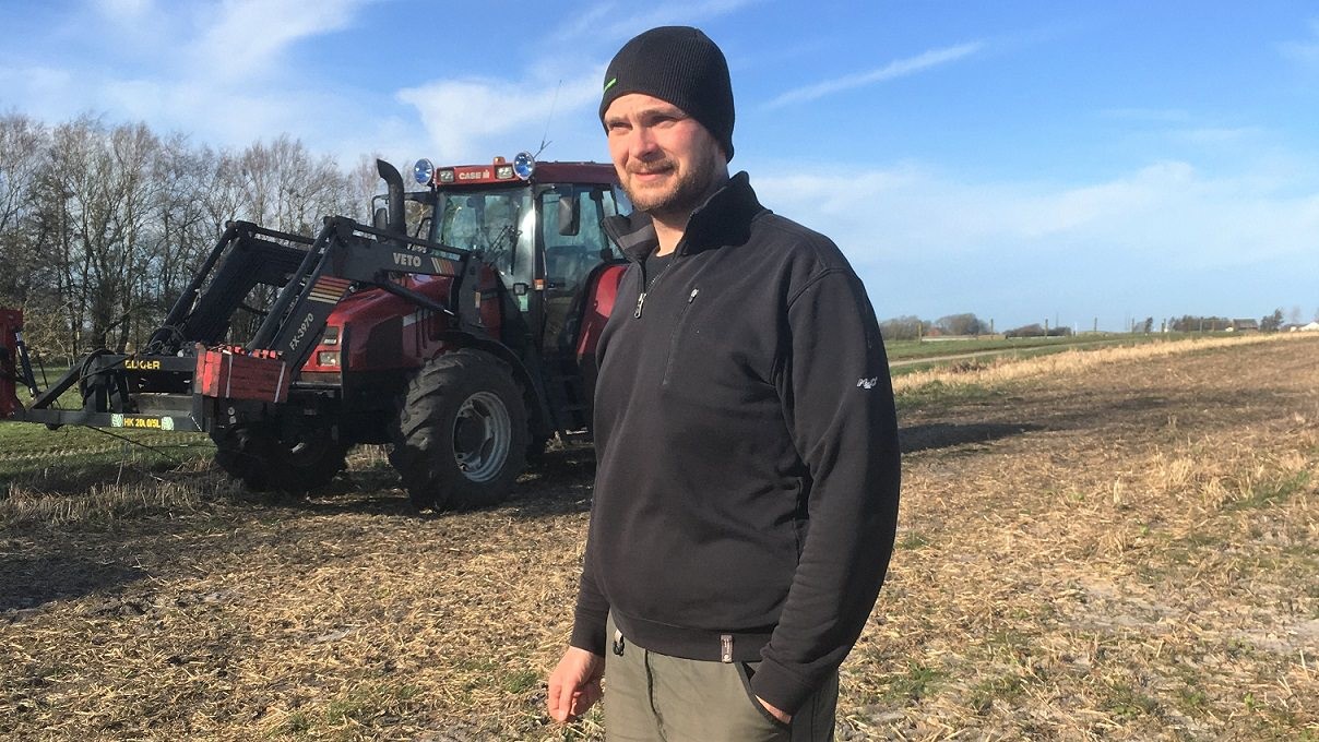 Søren Sandgaard på sin mark med en traktor i baggrunden