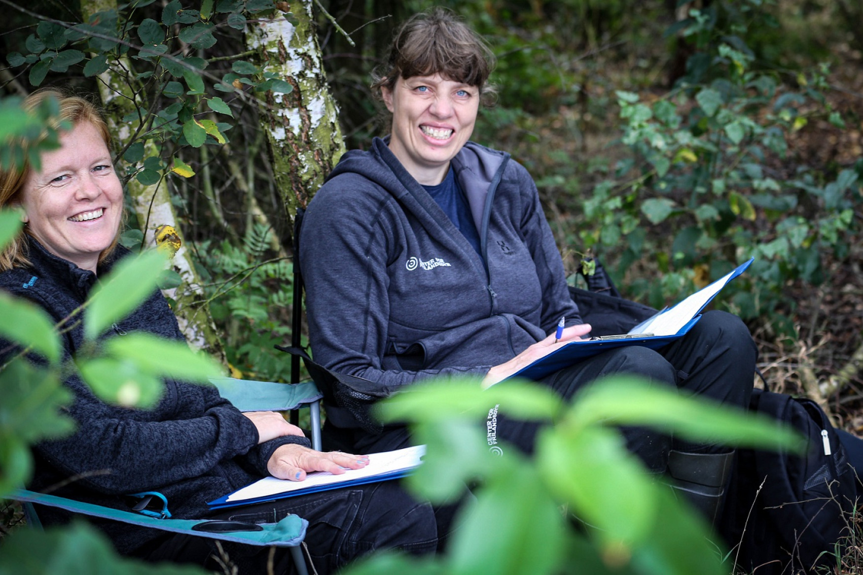 Rikke Thomsen og Kirstine Flintholm Jørgensen sidder i skoven på stole og smiler til kameraet