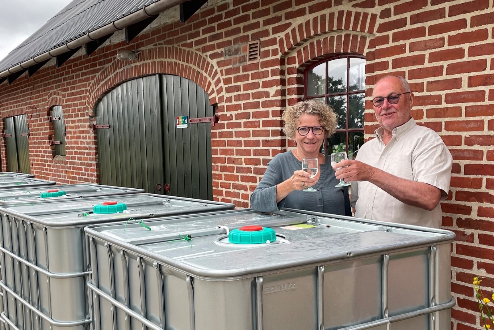 Lisbeth Haahr Sørensen og Jens Lindby Nielsen skåler bag de store palletanke med økologisk rom.