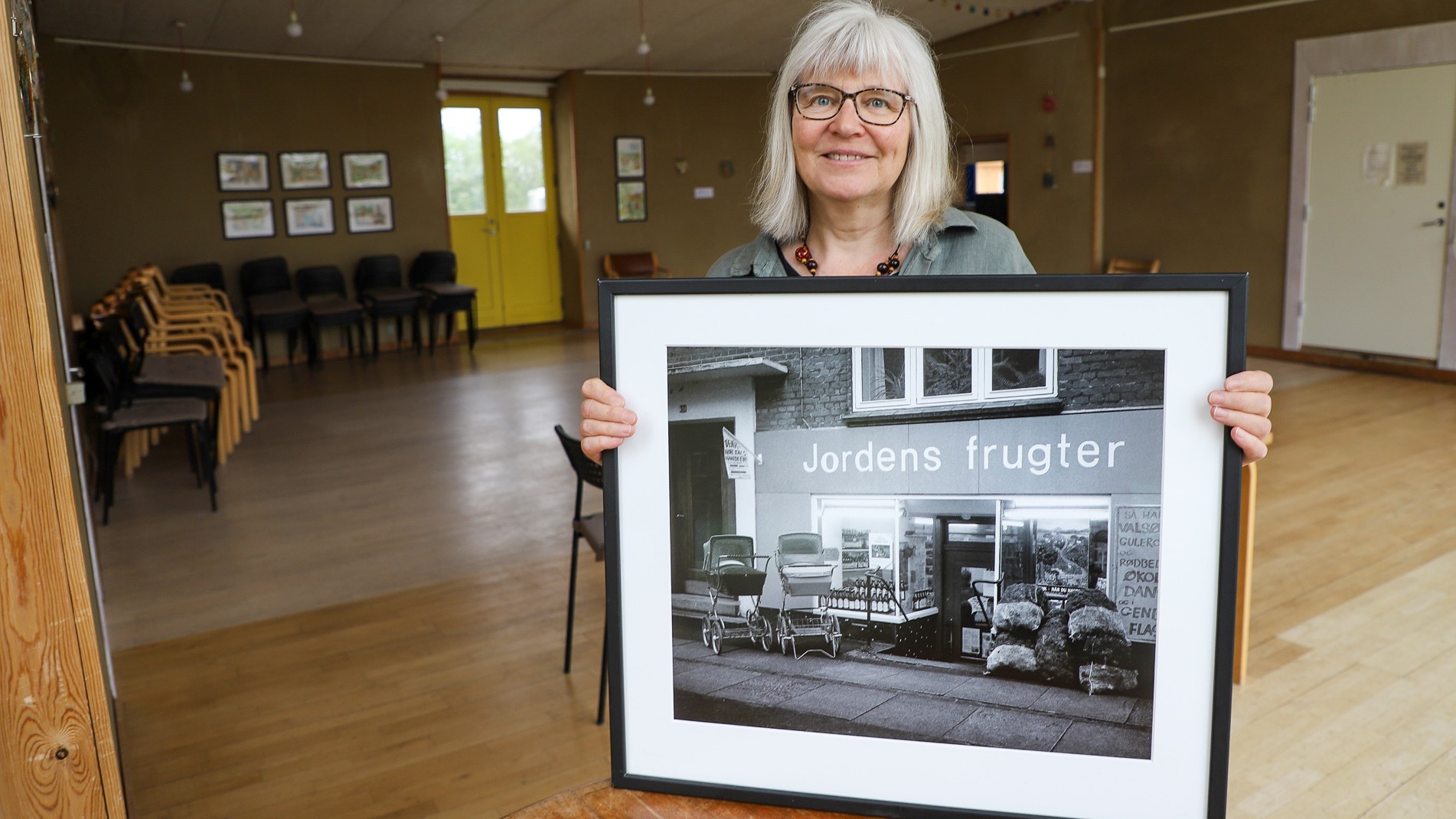 Bodil Dahl Jensen holder et stort portræt af Jordens Frugters første kælderlokale