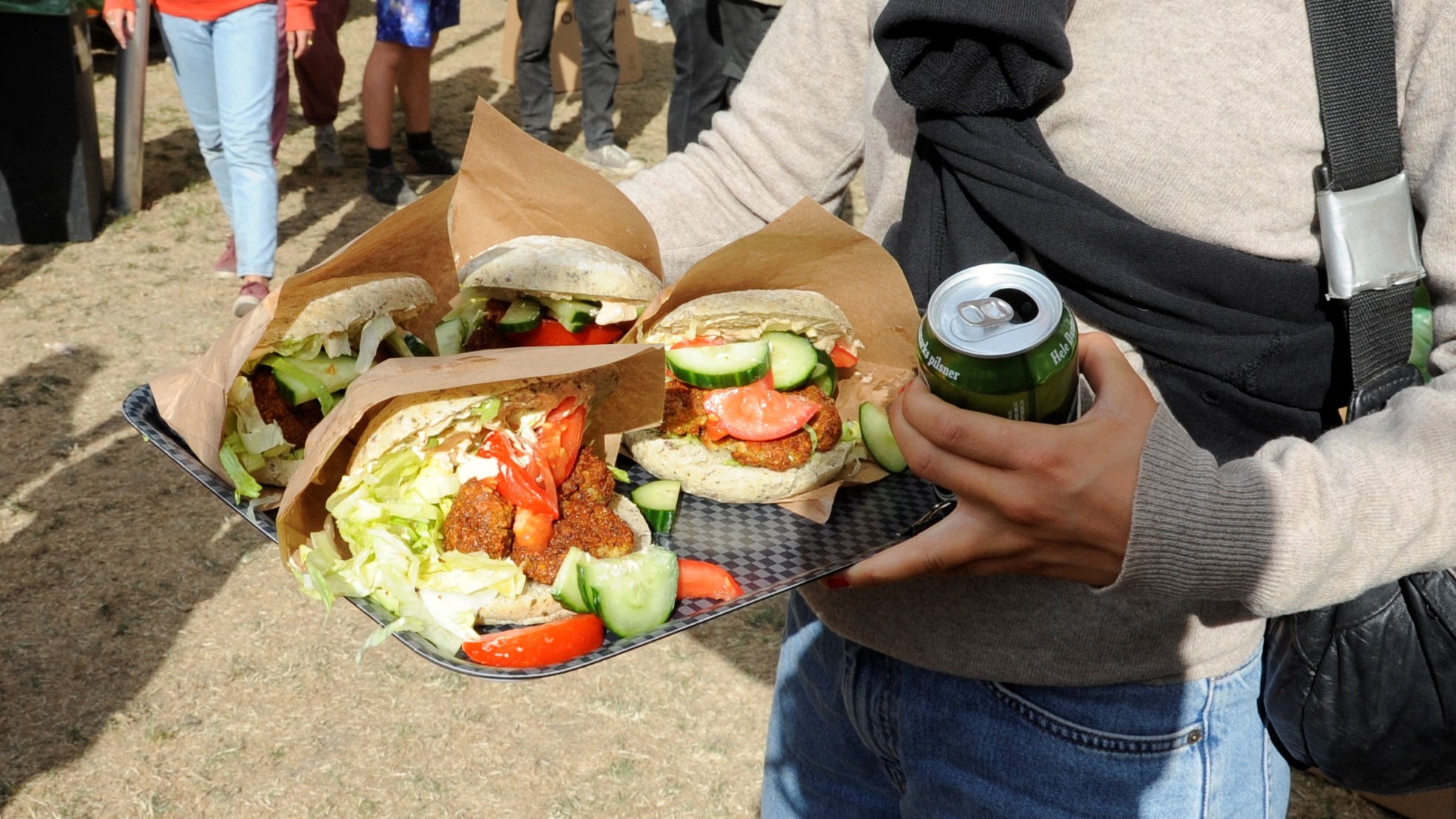 Festivaldeltager med bakke med planteburgere og en grøn tuborg