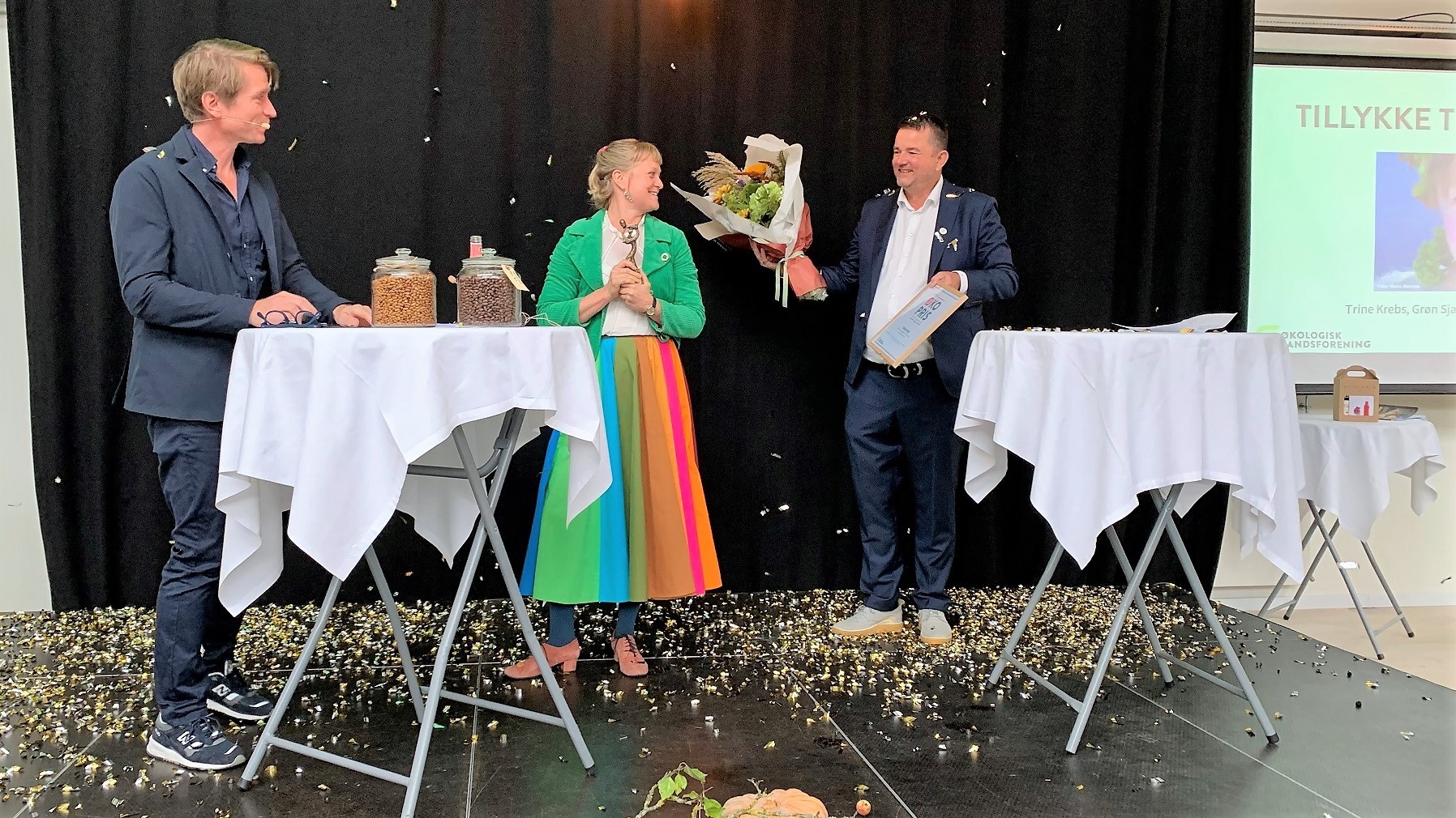 Trine Krebs står på scenen med Adam Aamann og Torben Blok og modtager prisen