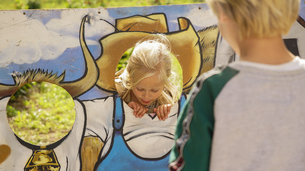 Børn leger med en malet træplade, hvor de kan stikke hovederne ud