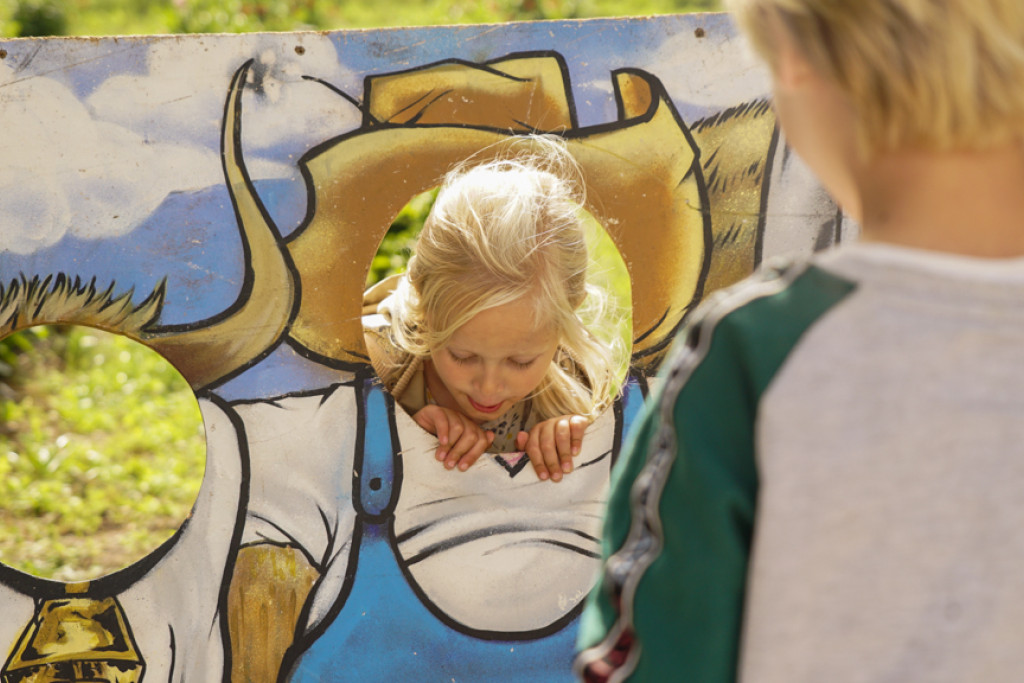 Børn leger med en malet træplade, hvor de kan stikke hovederne ud