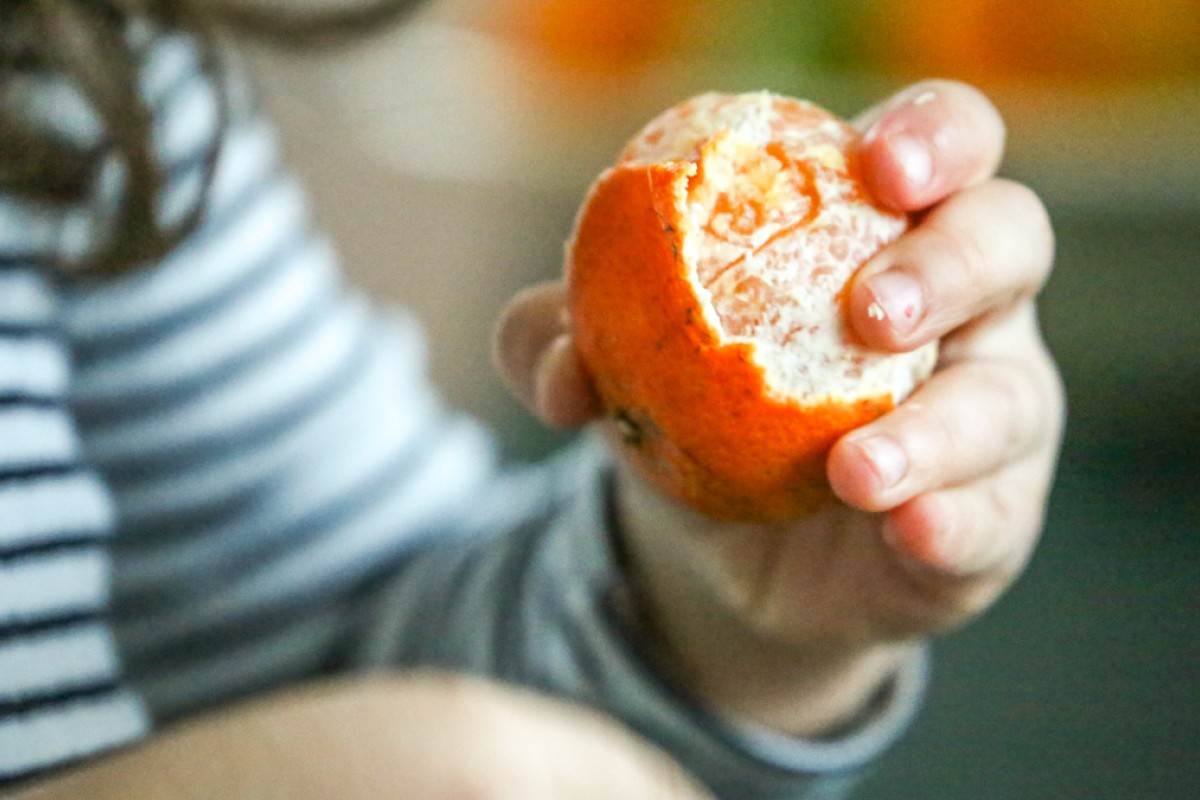 Et barn er ved at skrælle en klementin