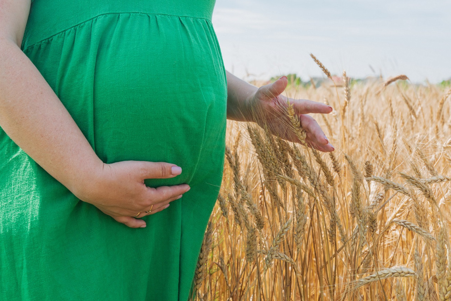 En gravid kvinde står i en kornmark