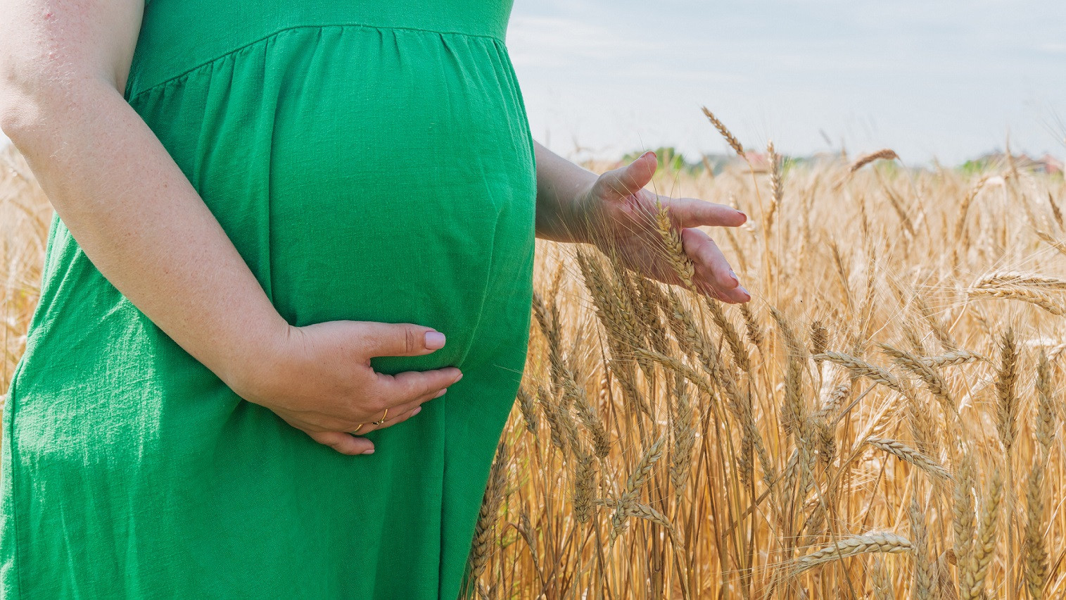 En gravid kvinde står i en kornmark