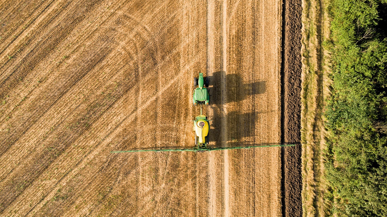 Luftfoto af traktor, der kører på en mark og sprøjter med pesticider