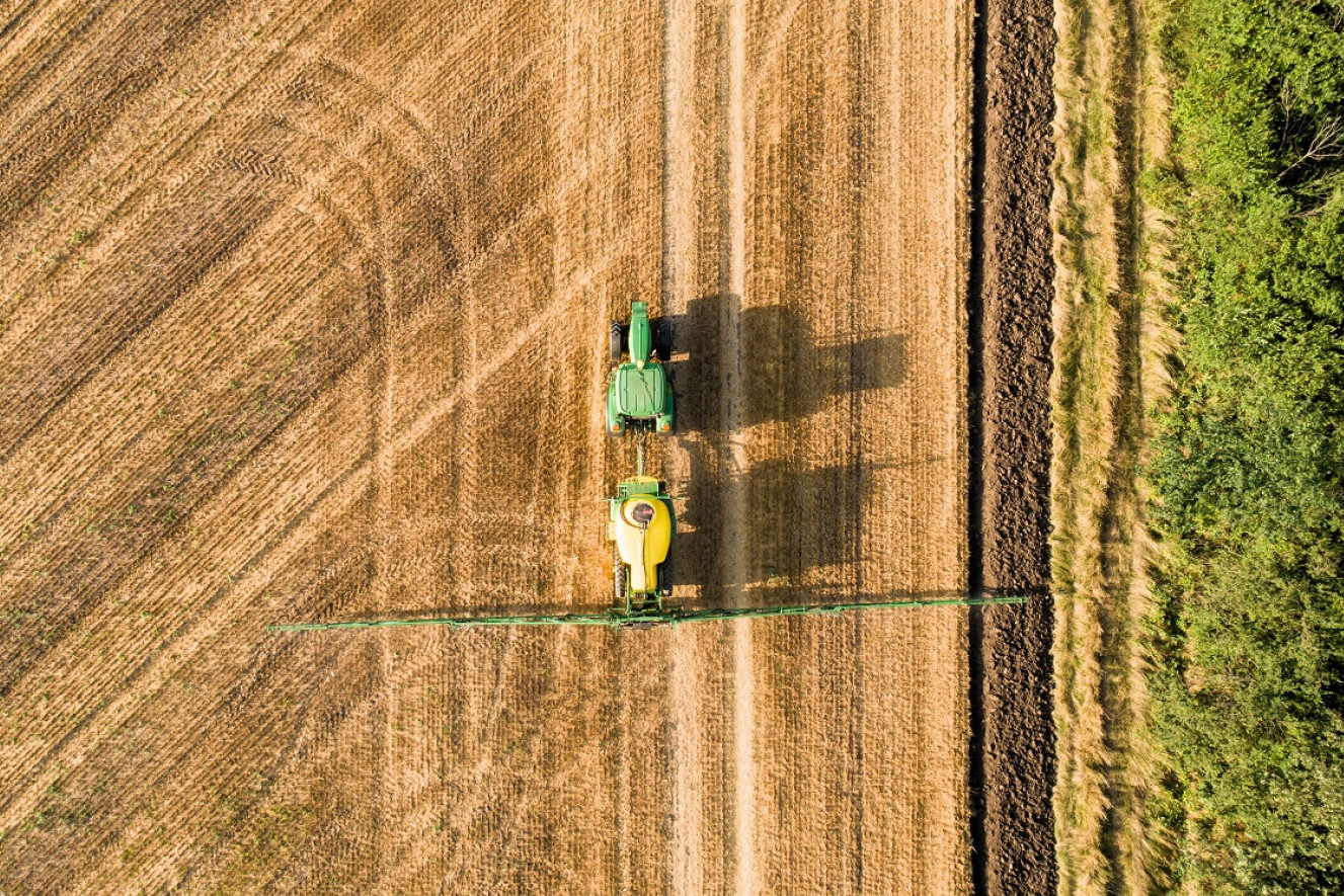 Luftfoto af traktor, der kører på en mark og sprøjter med pesticider