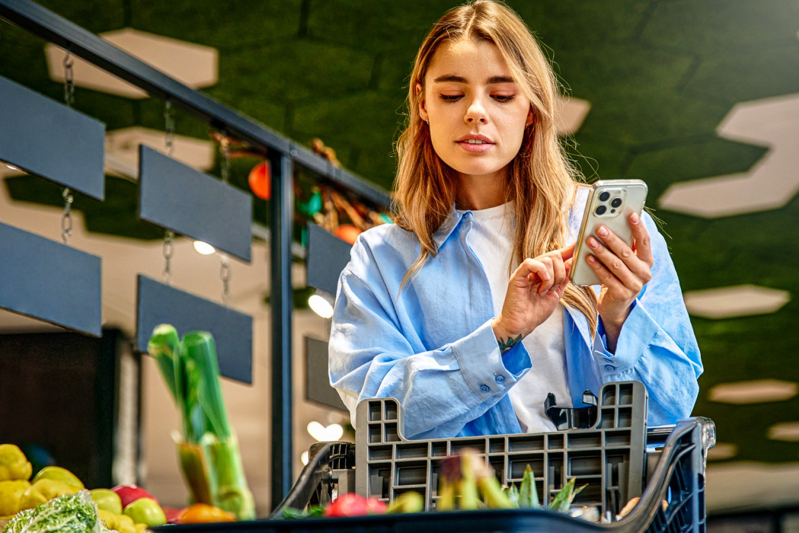 En kvinde står i et supermarked og bruger sin mobil