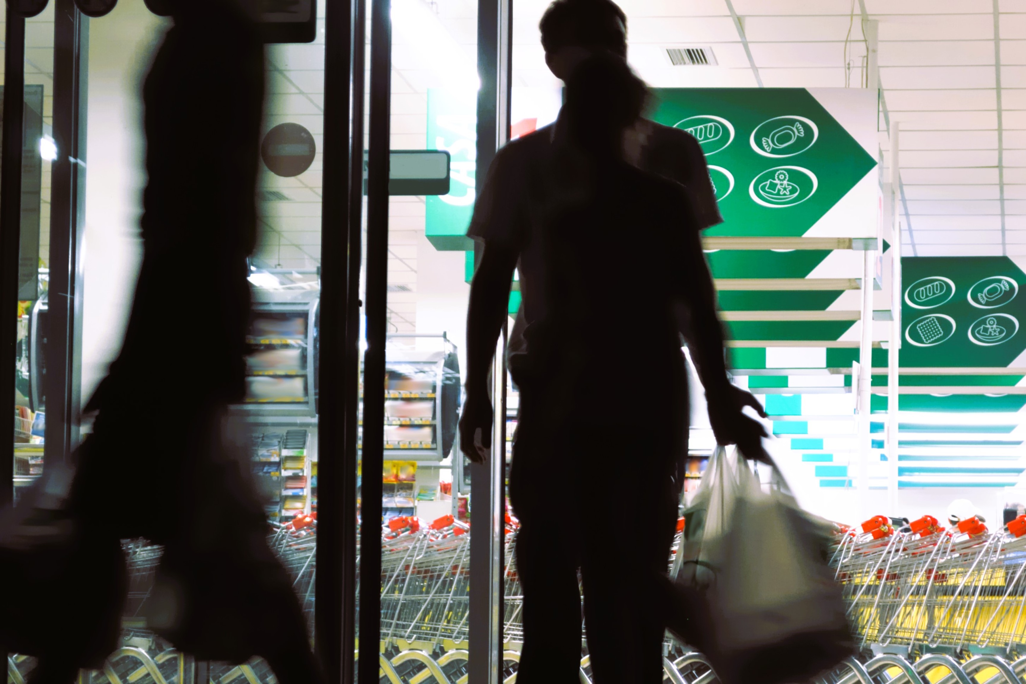 Silhuetter af personer, som går ind og ud af et supermarked