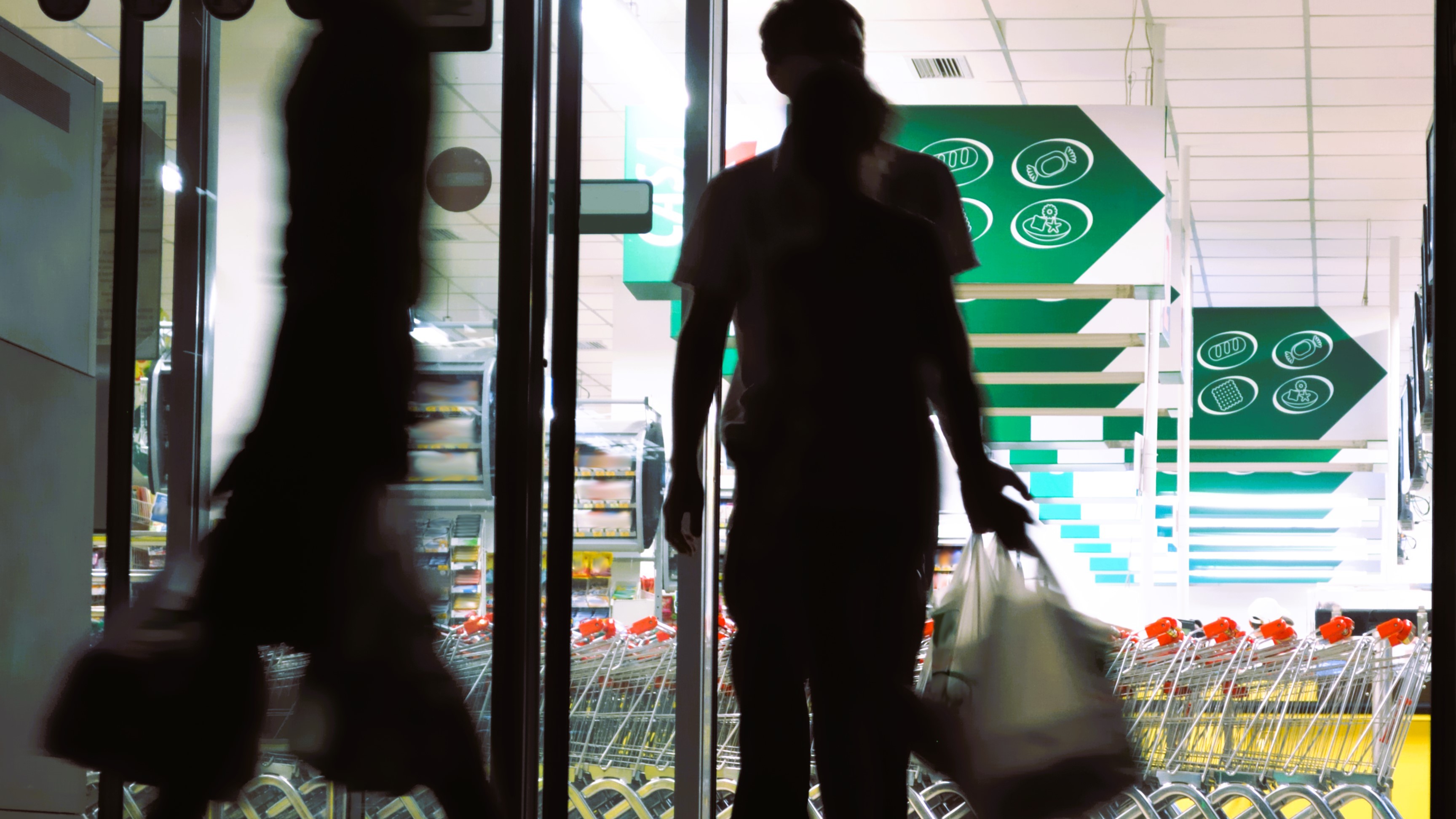 Silhuetter af personer, som går ind og ud af et supermarked
