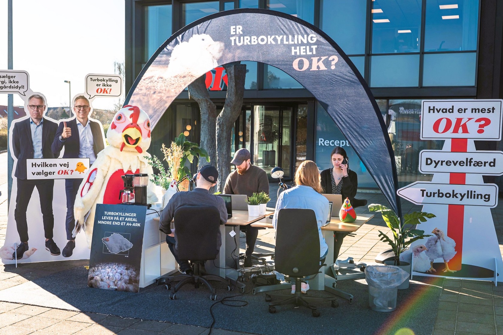 Anima-folk sidder foran OK's hovedkvarter med bannere og kaffe