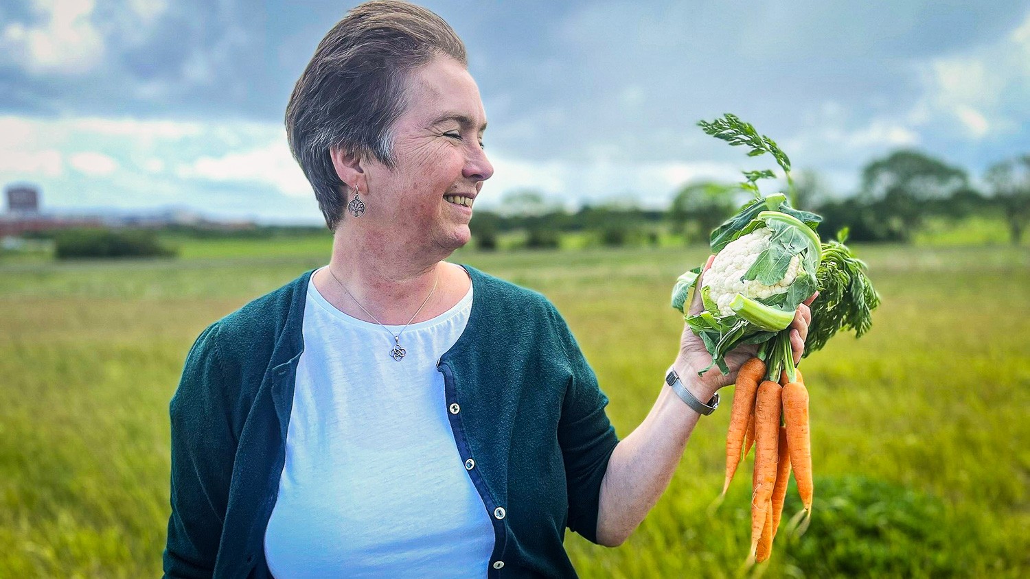 Hanne Lakkenborg Kristensen står på en mark med et blomkål og et bundt gulerødder i hånden