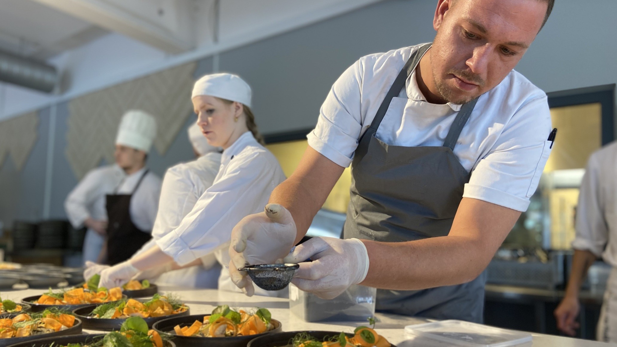 Kokkeelever anretter tallerkener med grøn mad