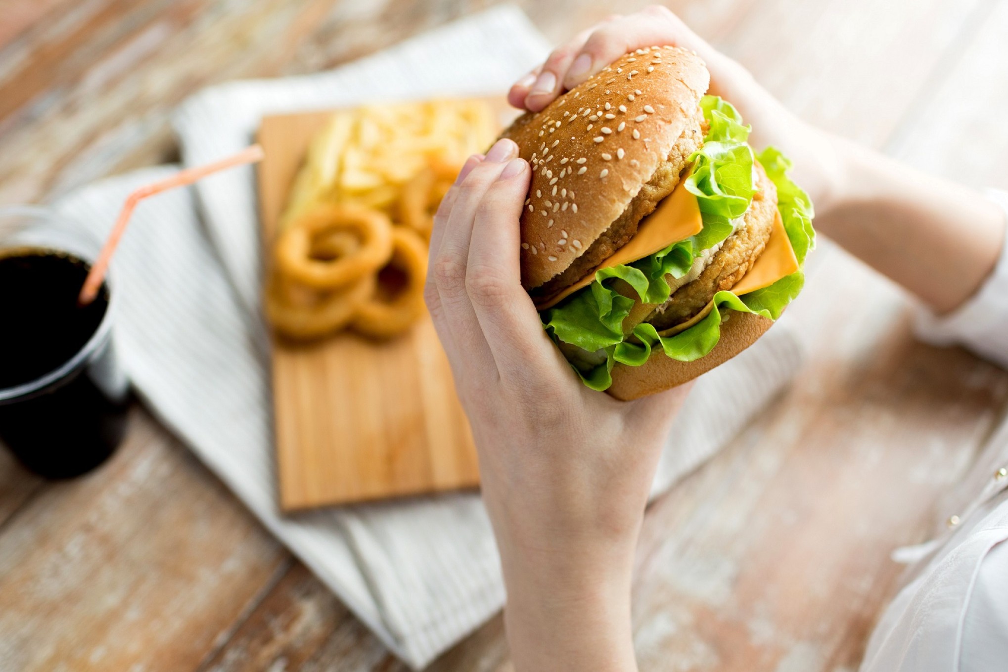 En person holder en cheeseburger med to bøffer - på bordet er en cola og onion rings