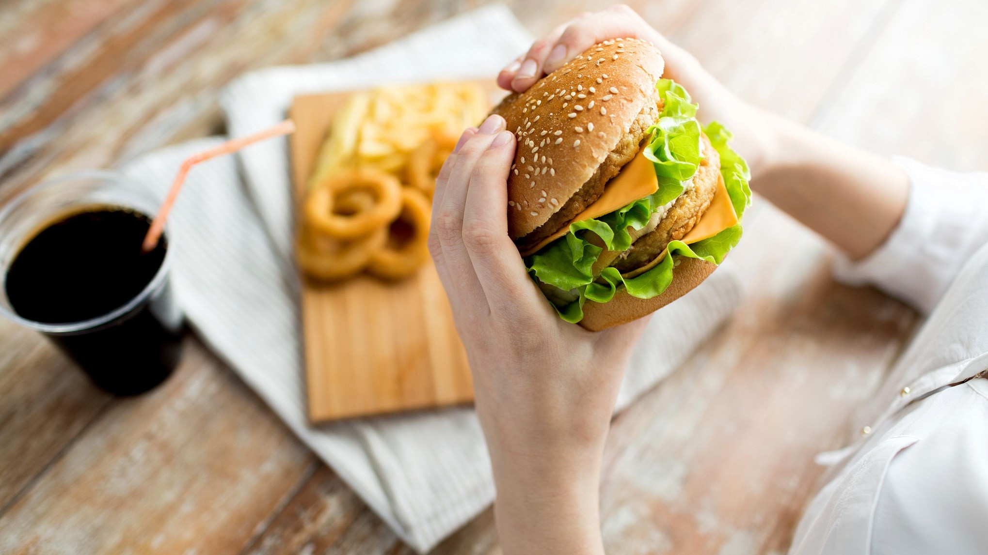 En person holder en cheeseburger med to bøffer - på bordet er en cola og onion rings