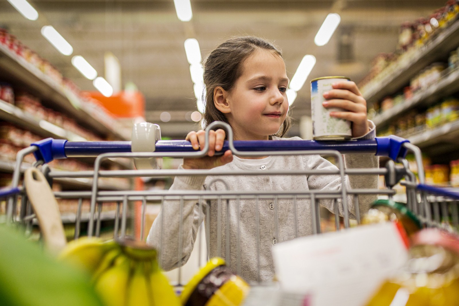 En pige går med en indkøbsvogn og holder en konservesdåse i hånden