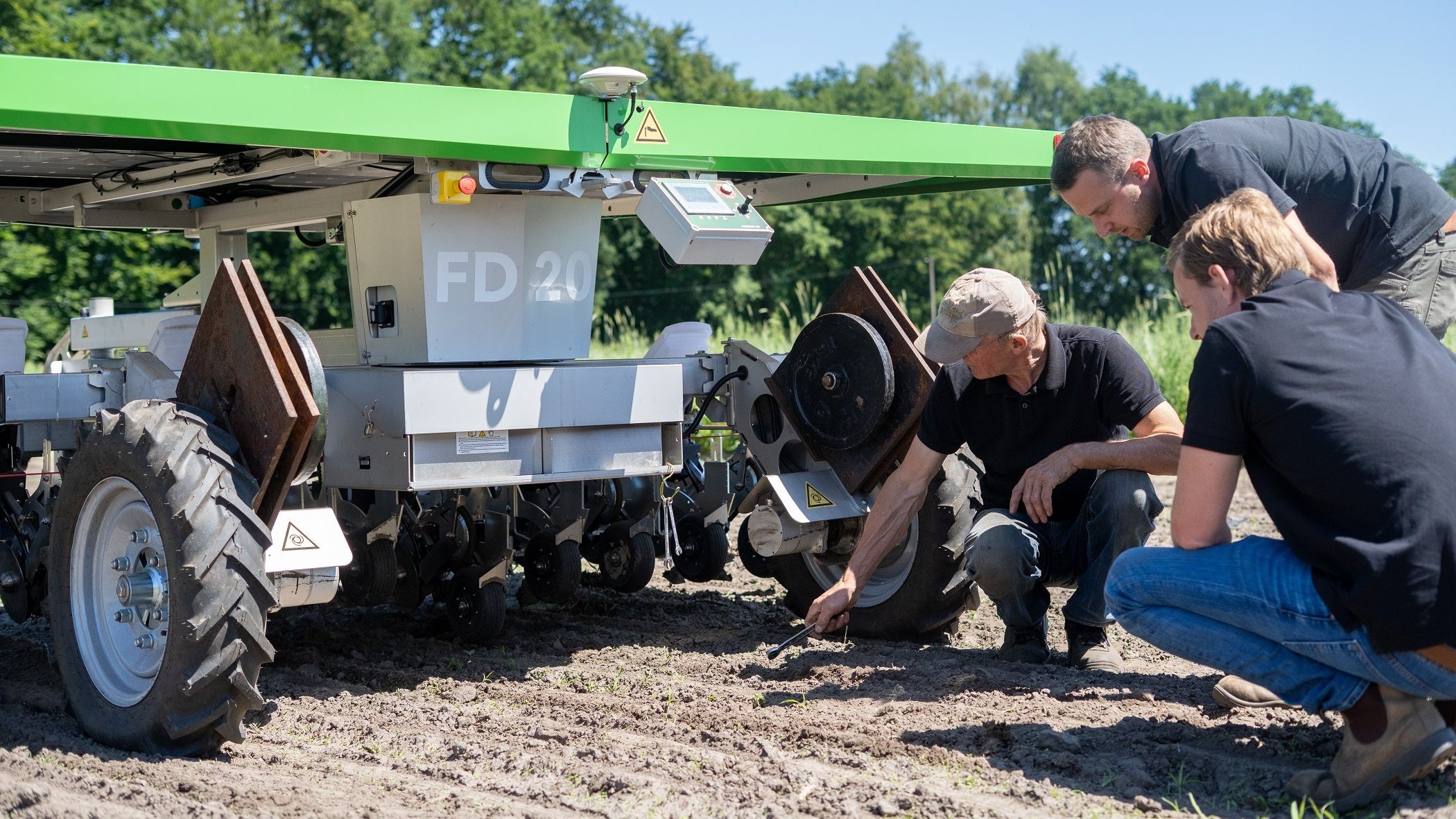 Ny Farmdroid ses an på marken - Nils Massmann står foroverbøjet, hans far sidder på hug t.v. og en sælger fra Farmdroid sidder til højre