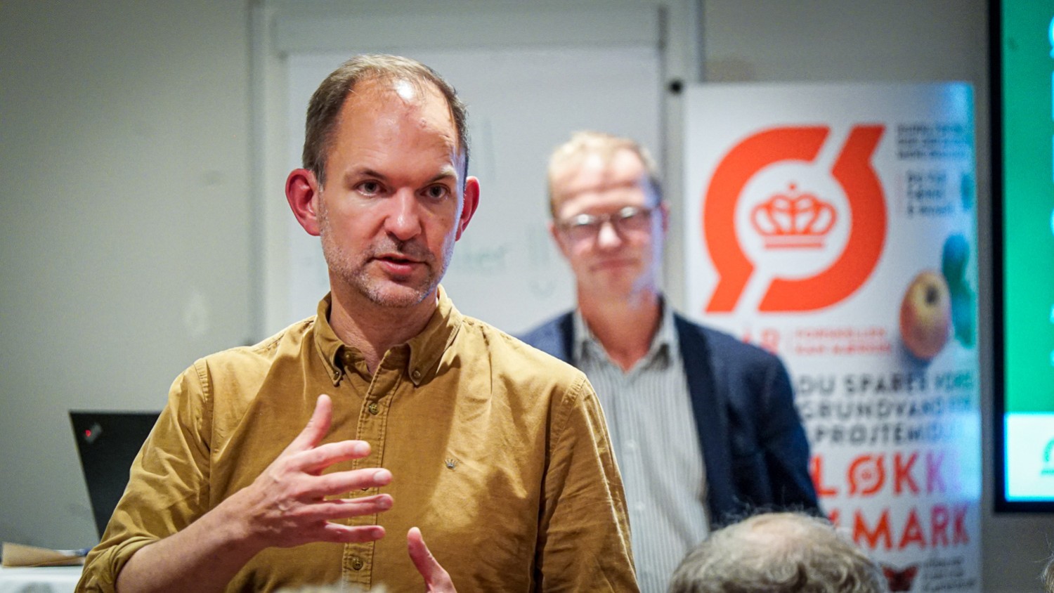 Jeppe Bruus taler til medlemsmøde i Middelfart 2025 - Johannes Lundsfryd Jensen står i baggrunden