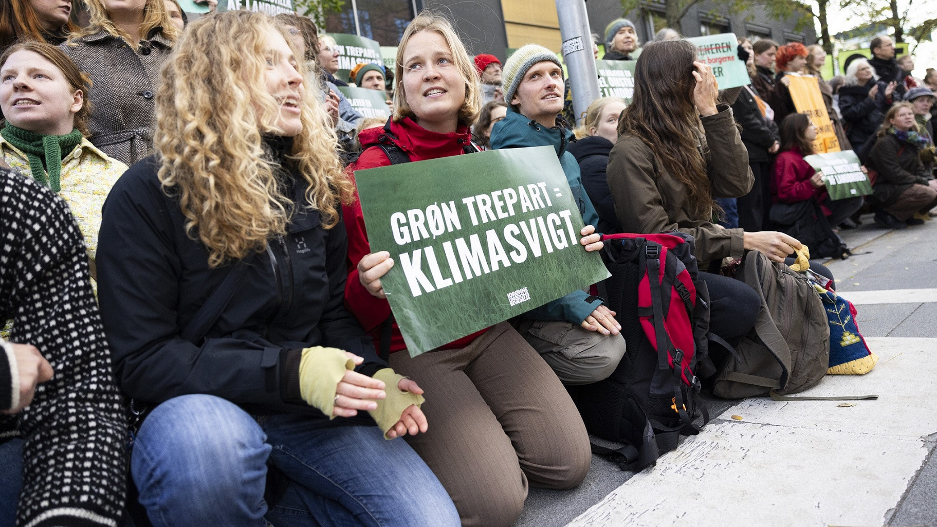 Unge sidder på hug i protest - en sidder med et skilt med teksten 