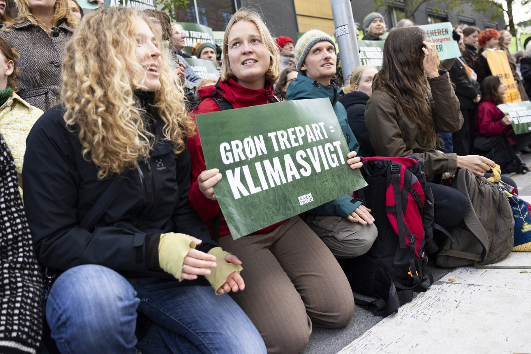 Unge sidder på hug i protest - en sidder med et skilt med teksten 